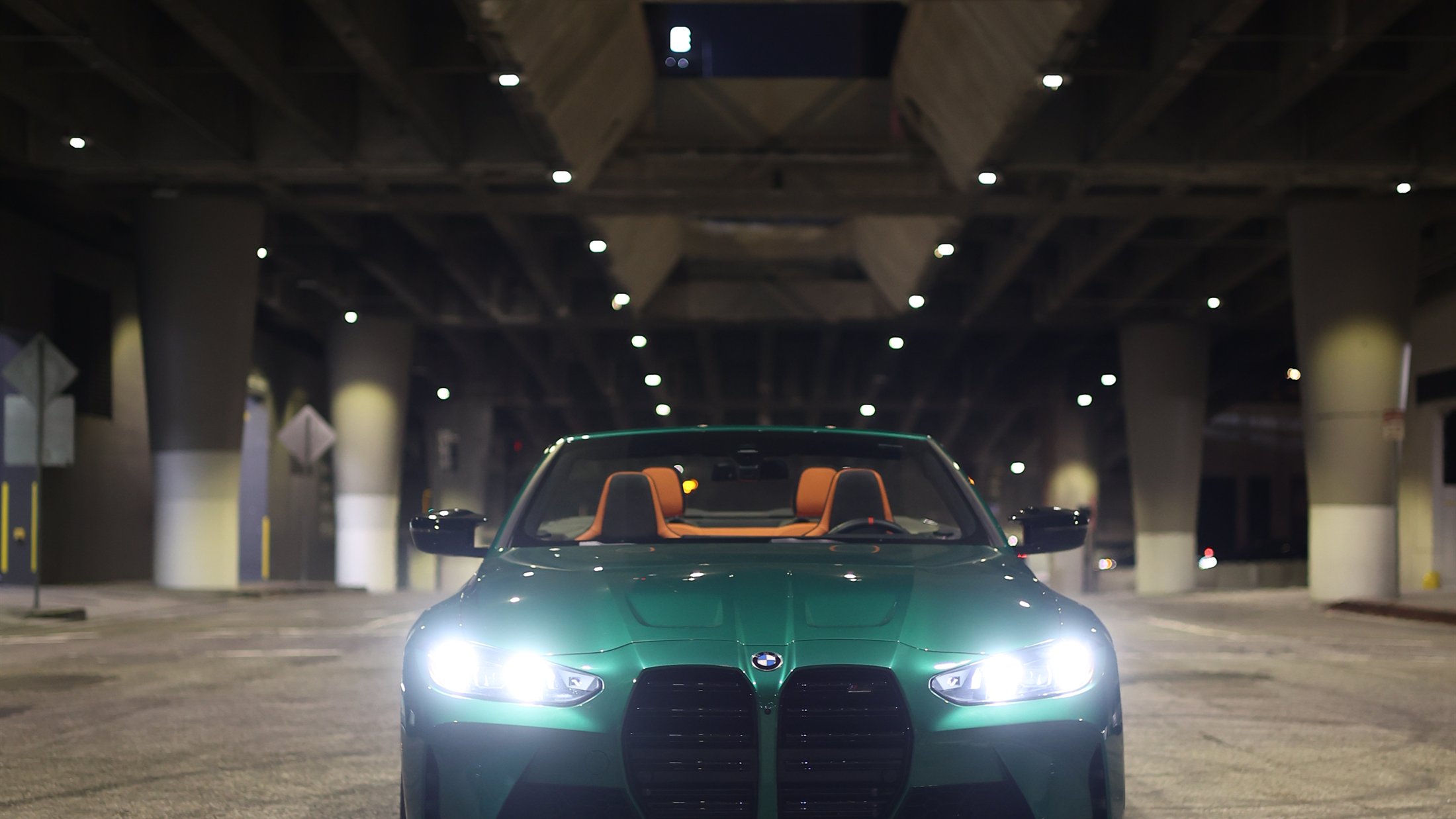 Green BMW M4 convertible with headlights on in a dark parking structure
